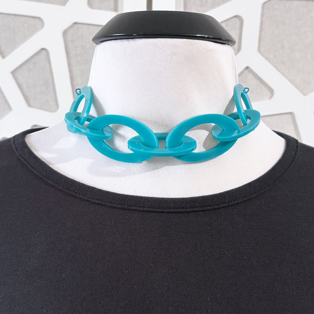 Teal chain necklace on a mannequin with a black top against a geometric patterned background